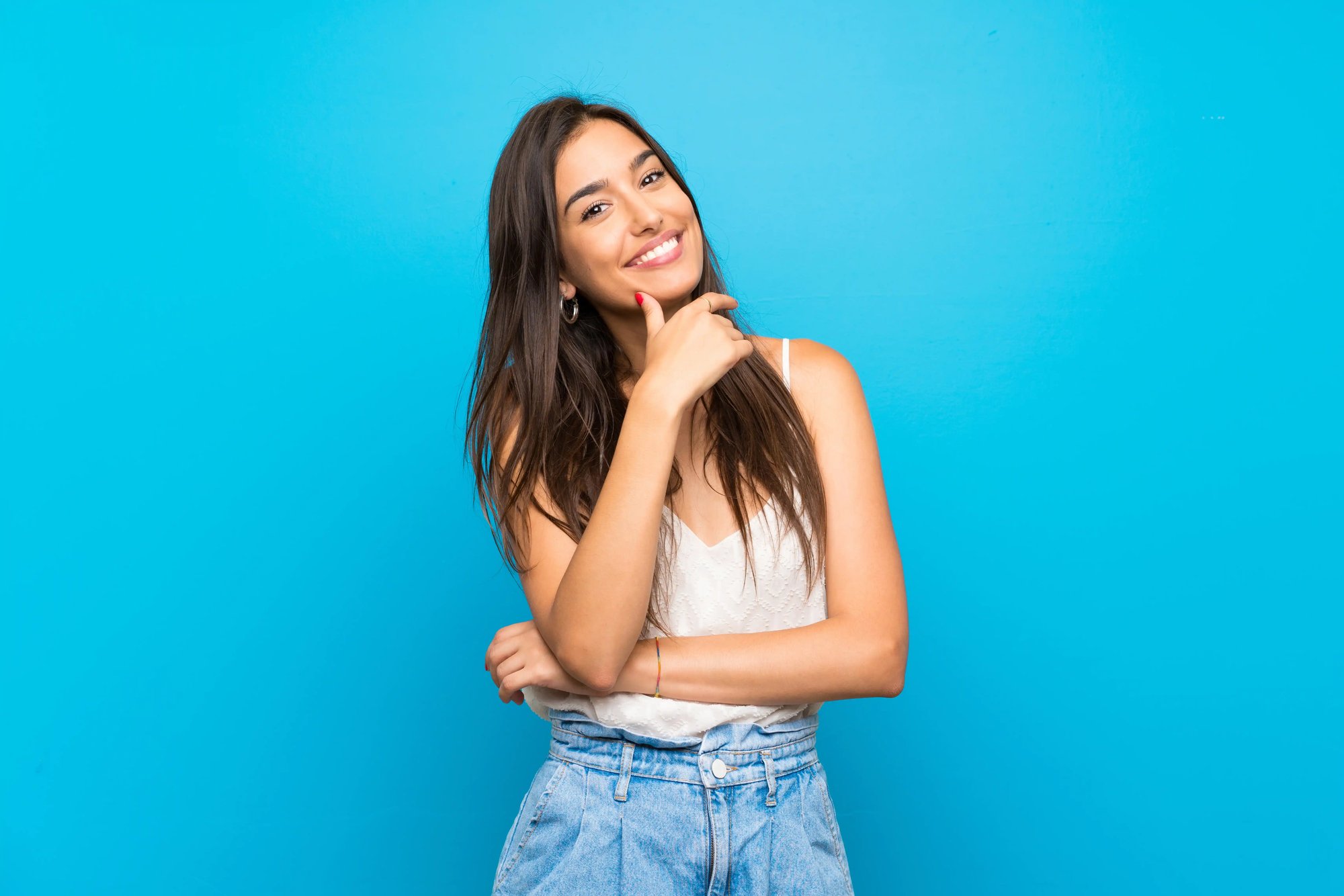 Foto ilustrativa de estudio de archivo de una mujer sonriente sobre un fondo cian con un dedo cerca del mentón; no muestra pacientes de Leva